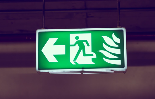 Green emergency fire exit sign with arrow pointing left and running figure.
