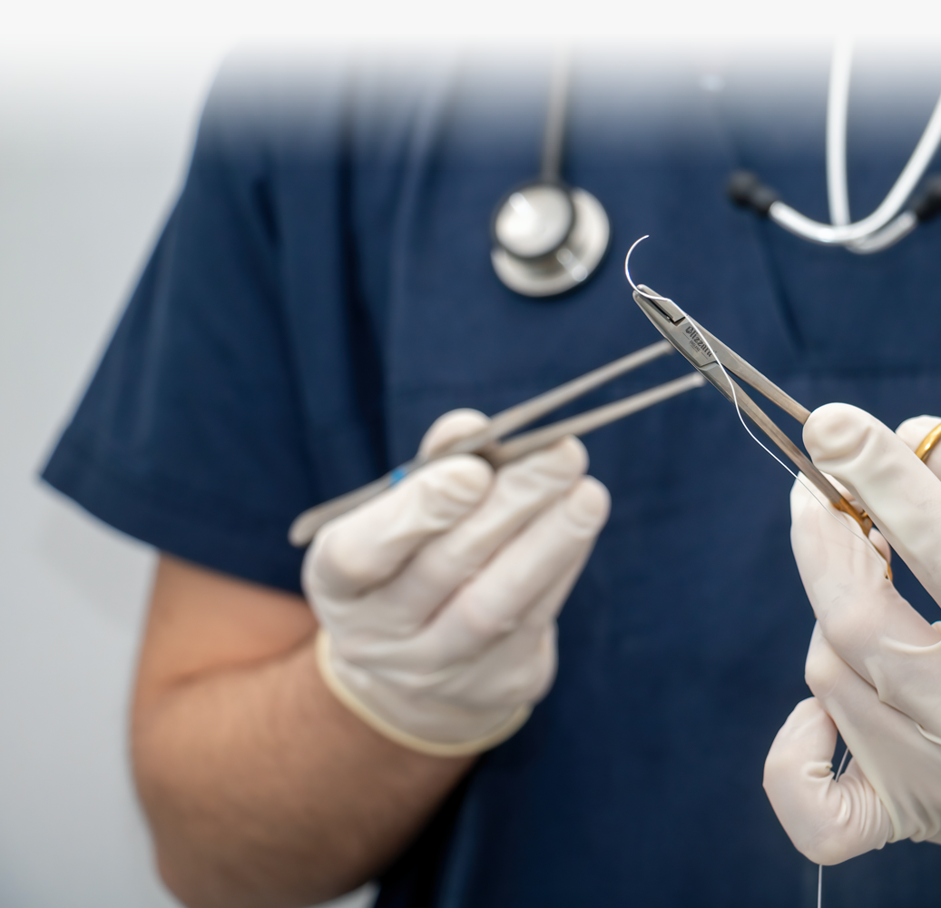 Medical professional holding needle holders and forceps while preparing a curved suture needle